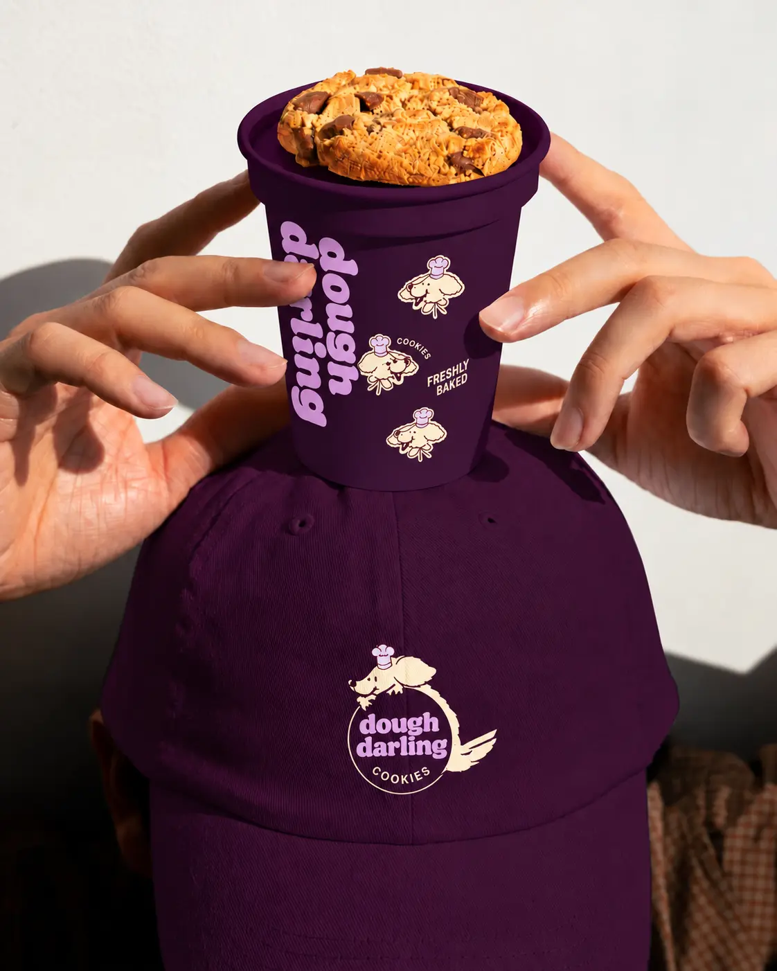 A Dough Darling cookie resting on a branded plum cup balanced on a matching cap