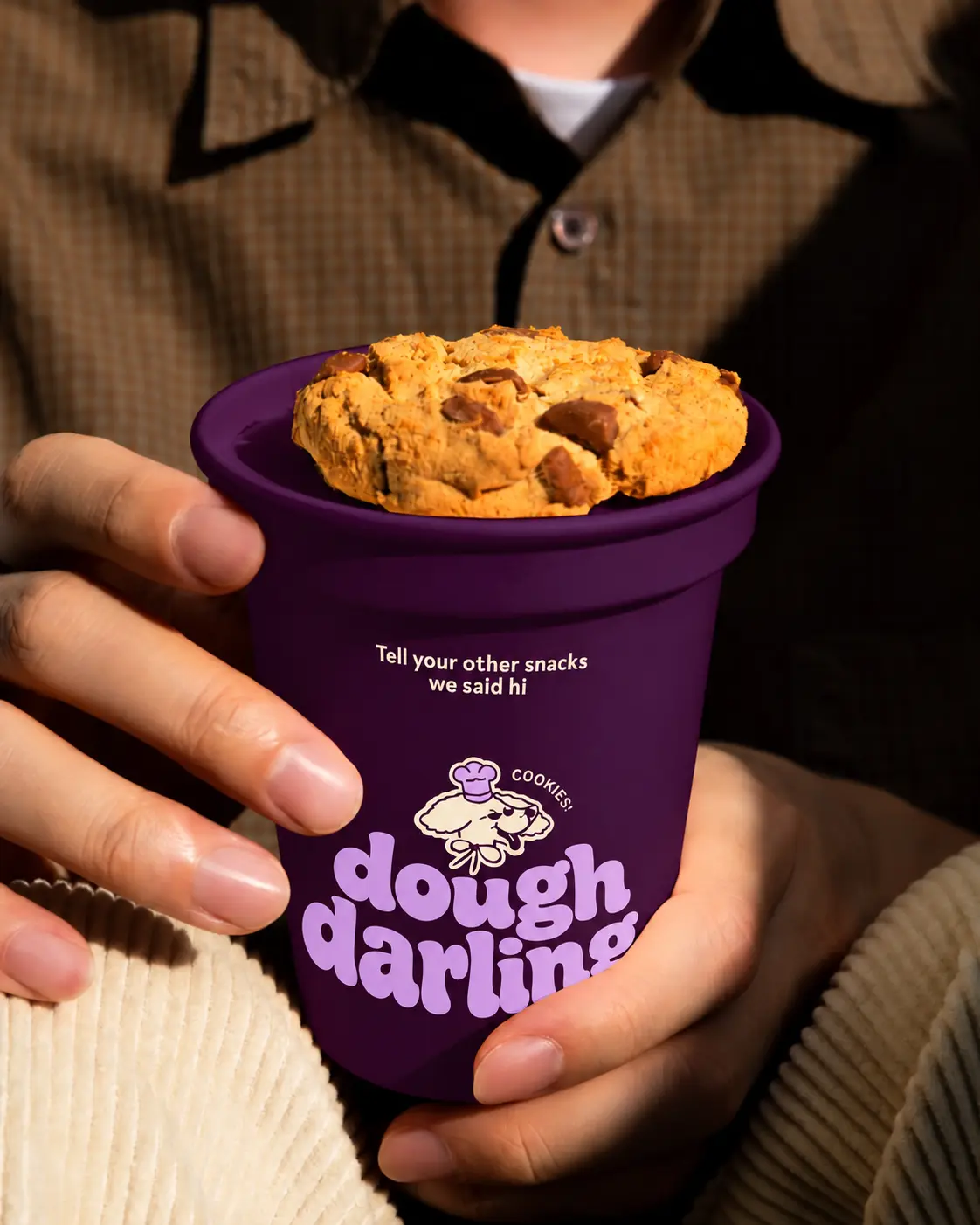 Hands holding a Dough Darling plum cup topped with a chocolate chip cookie
